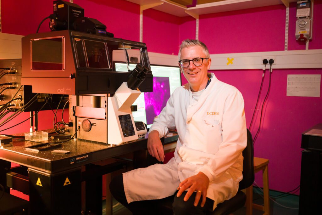 Professor David Hodson in his lab, sitting next to a microscope