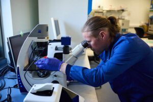 Dr Craig Beall wearing a lab coat and looking into a microscope