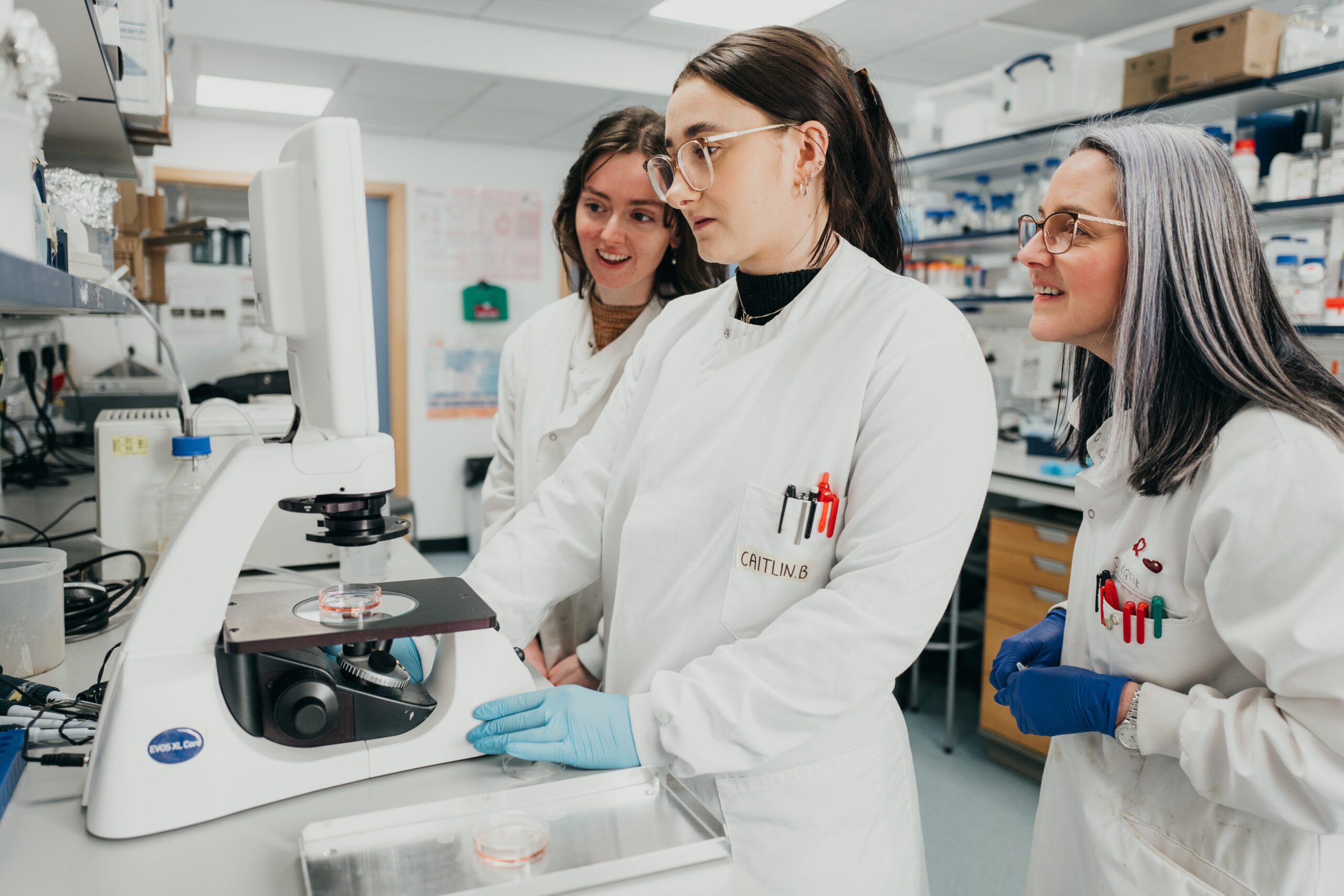 Researchers in lab coats looking at a screen together in their lab