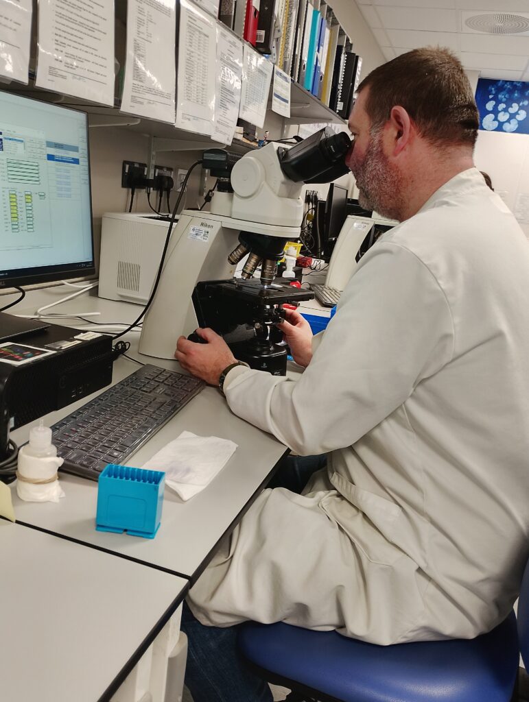 Man sat in laboratory looking down microscope